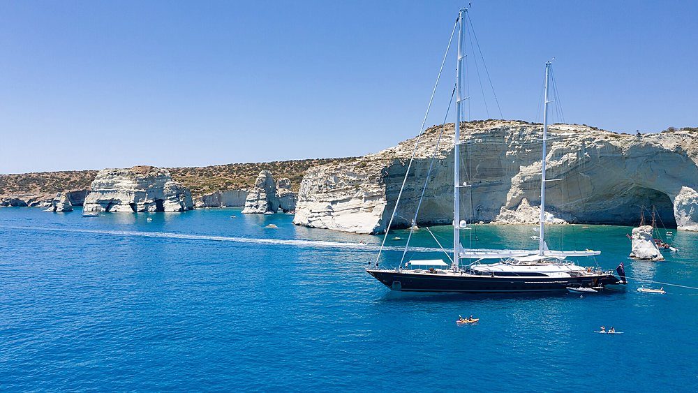 A sailing yacht at anchor in a cliff-walled bay, seen from above